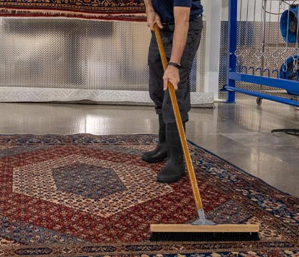 professional worker cleaning rug with broom brush